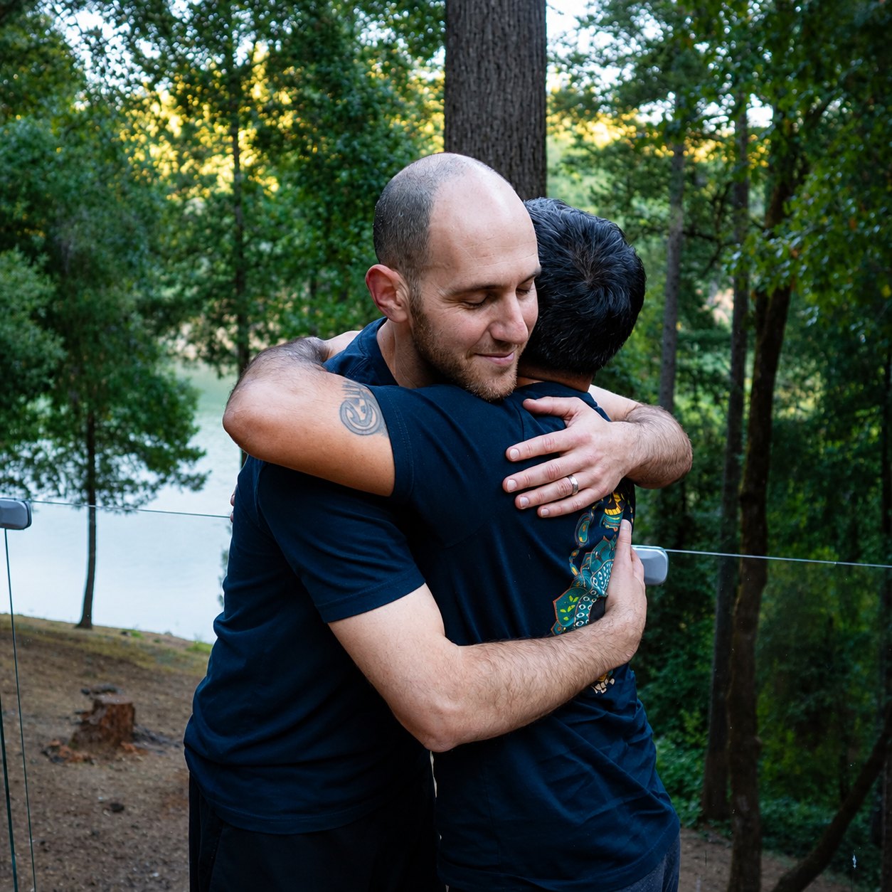 Two men embracing at a retreat, lake and trees behind them